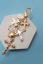 Load image into Gallery viewer, Keychain with gold cross pendants with various designs on a hexagonal stone surface against a blue background