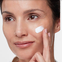 Load image into Gallery viewer, Woman applying SPF to her face with a neutral background

