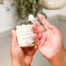 Load image into Gallery viewer, Person holding a jar of body crème with a blurred natural background
